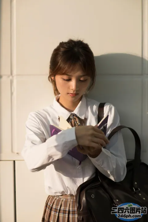 有一个女人站在墙边，手里拿着一个袋子