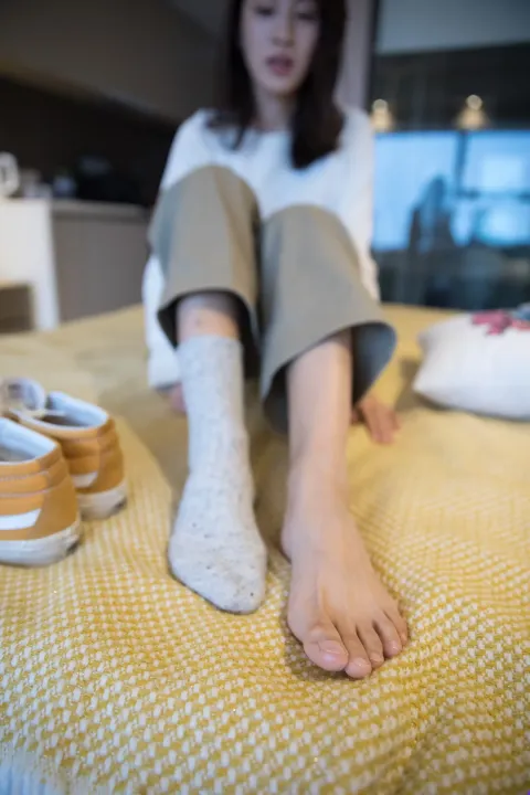 有一个女人坐在床上，双脚抬起