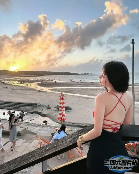 身穿红色连衣裙的 araffe 女子站在俯瞰海滩的阳台上