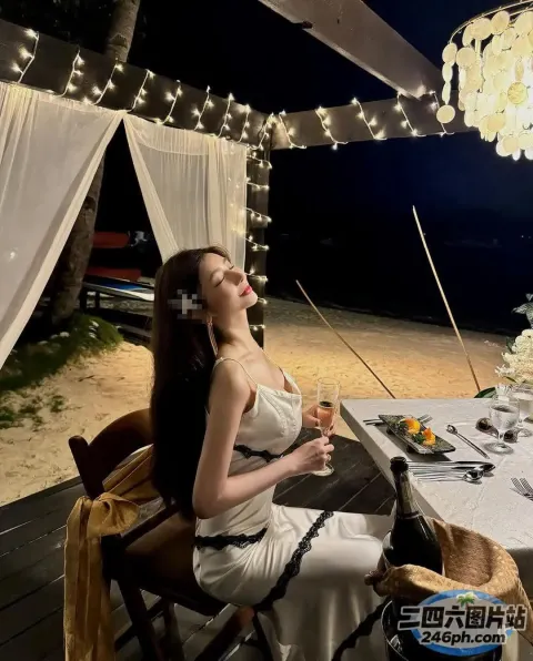 有个女人坐在桌子旁，手里拿着一杯酒