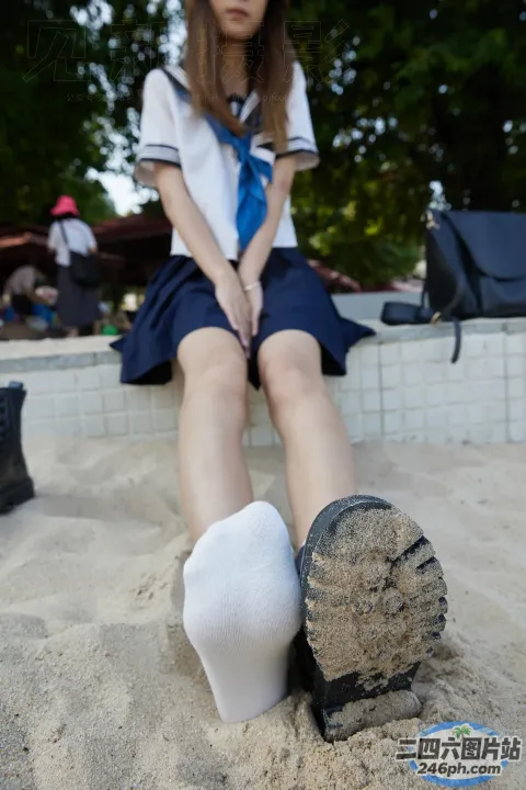 身穿制服的阿拉夫德女子坐在长凳上，双脚踩在沙子里