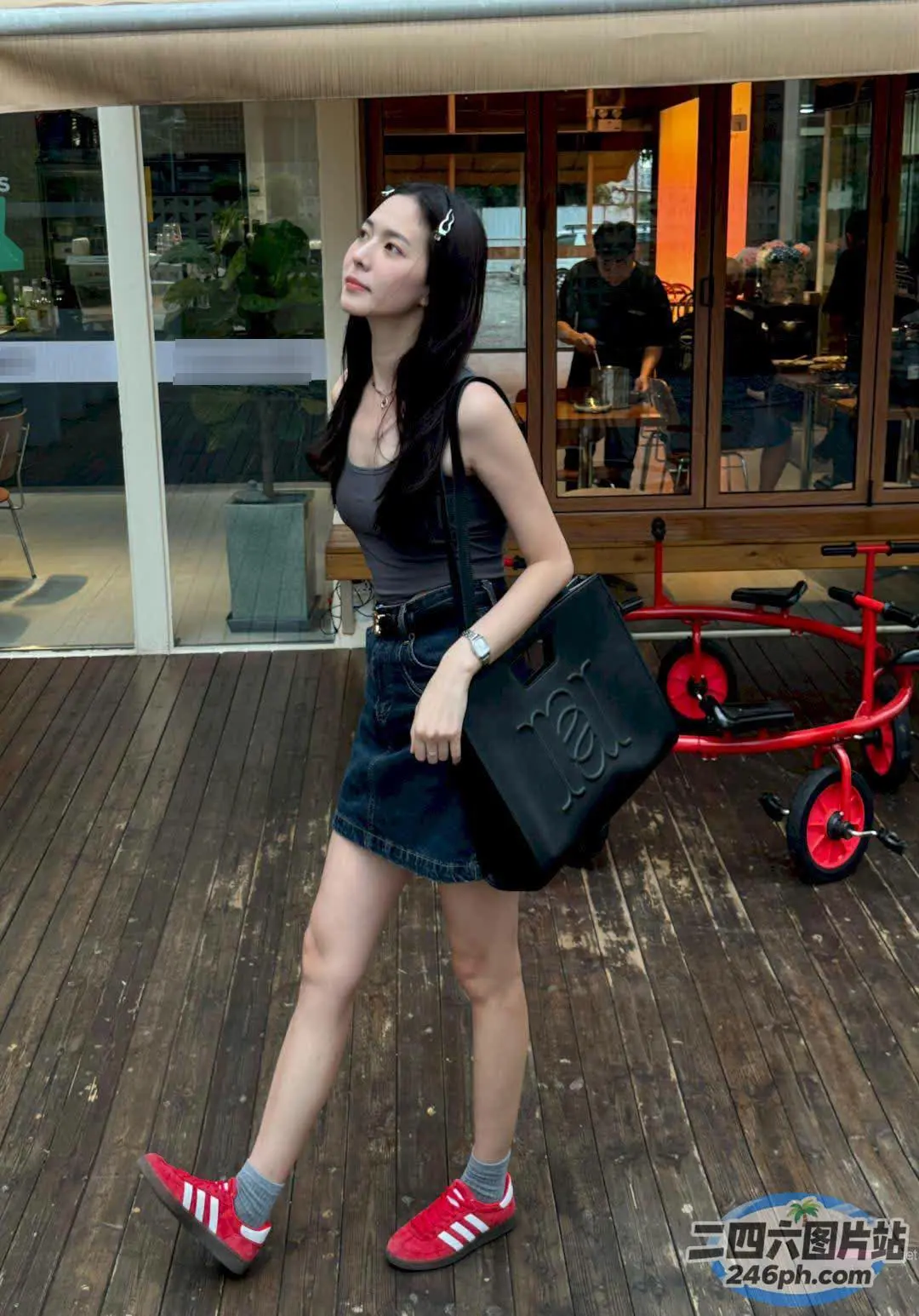 女人拿着一个黑色的包和红色的鞋子走在木甲板上