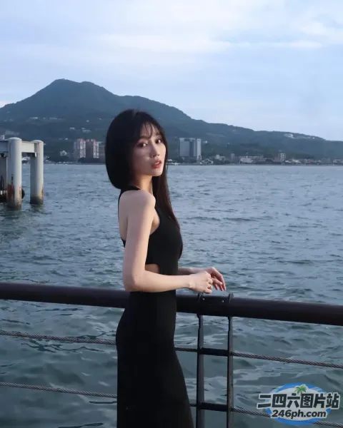 身穿黑色连衣裙的女子站在水体附近的栏杆上