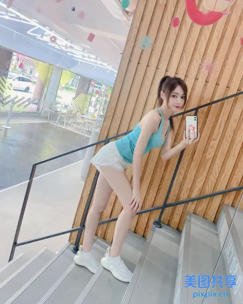身穿蓝色上衣和白色短裤的女子站在楼梯上，手里拿着手机