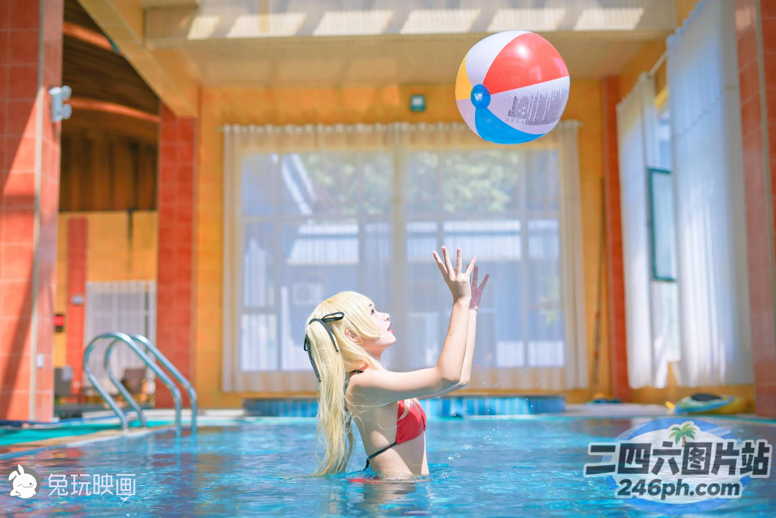 穿着红色比基尼的金发女子在泳池中玩沙滩球