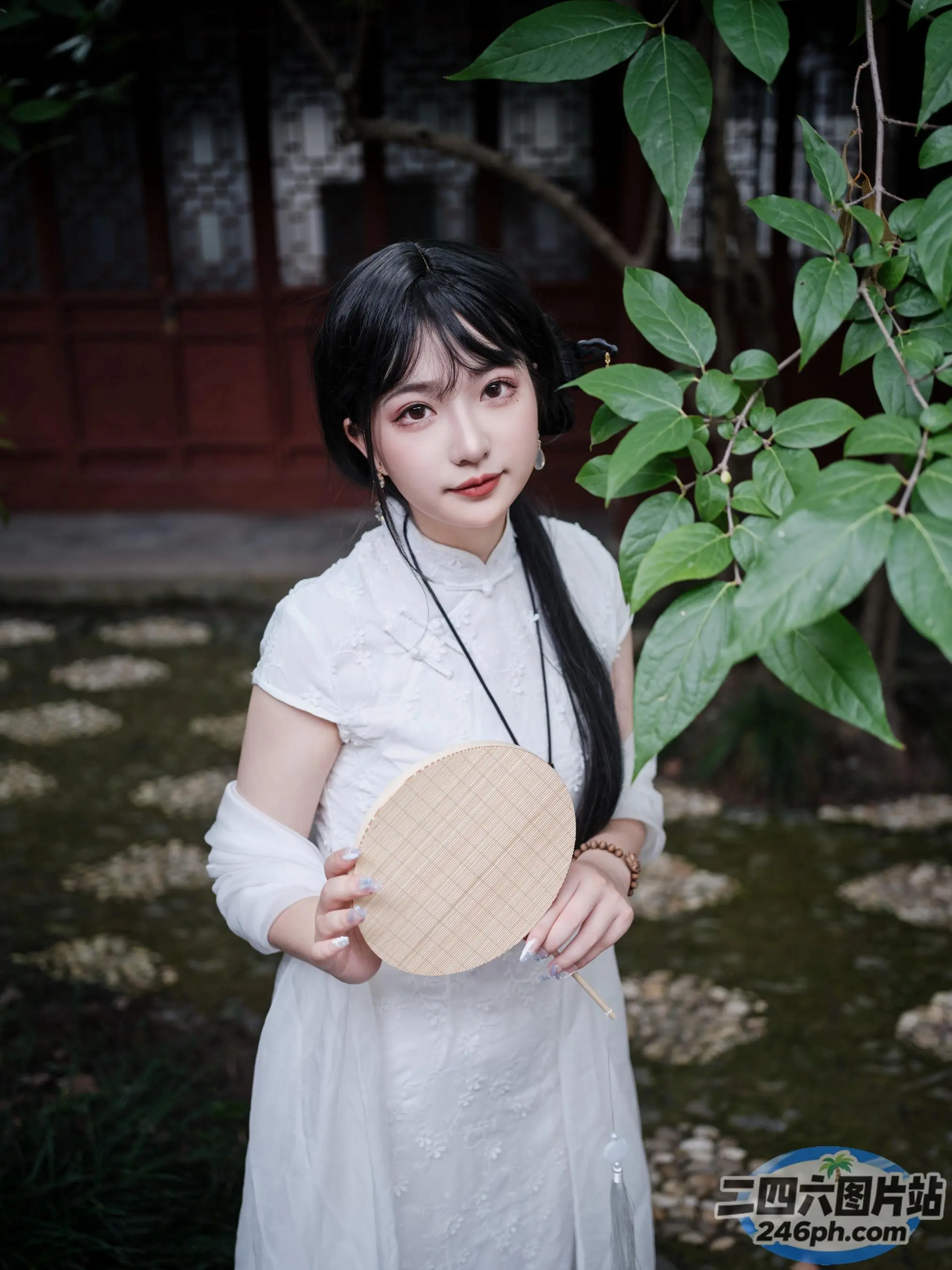 有个身穿白色连衣裙的女人，手里拿着一把木扇