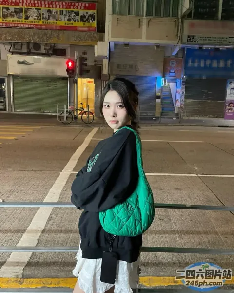 人行道上站着一个女人，手里拿着一个绿色的袋子