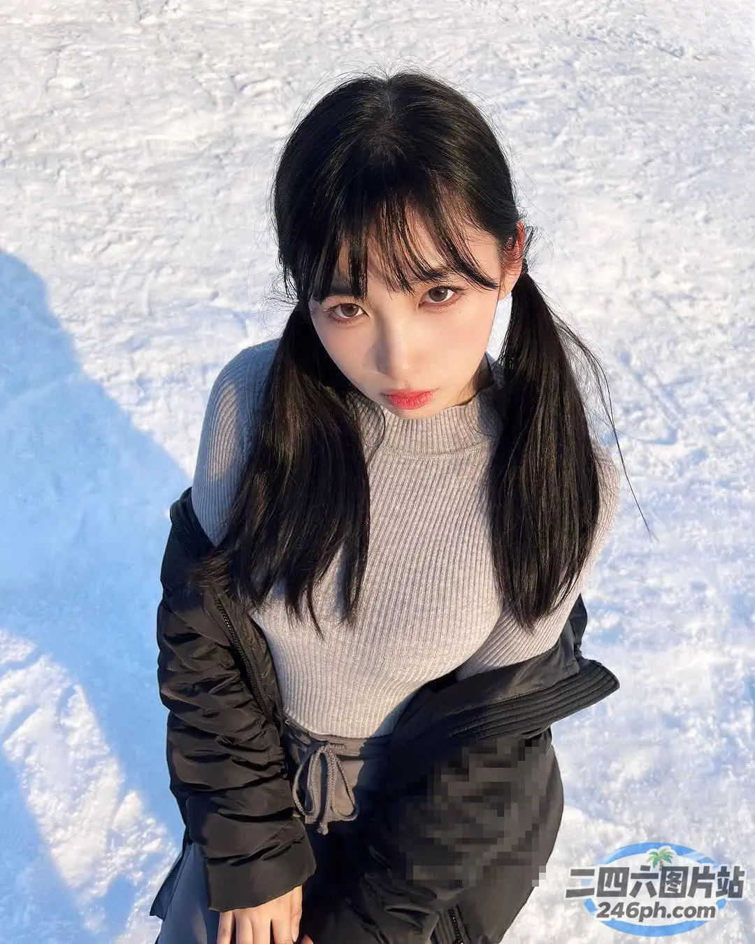 身穿黑色夹克和灰色毛衣的 Arafed 女子坐在白雪皑皑的地面上