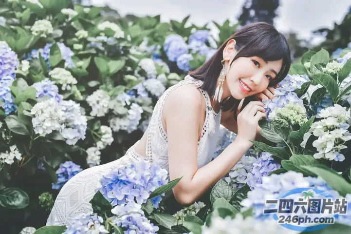 身穿白色连衣裙的 arafed 女子在蓝色花田中摆姿势