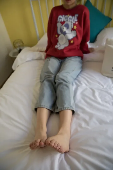 有一个年轻的女孩坐在床上，双脚抬起