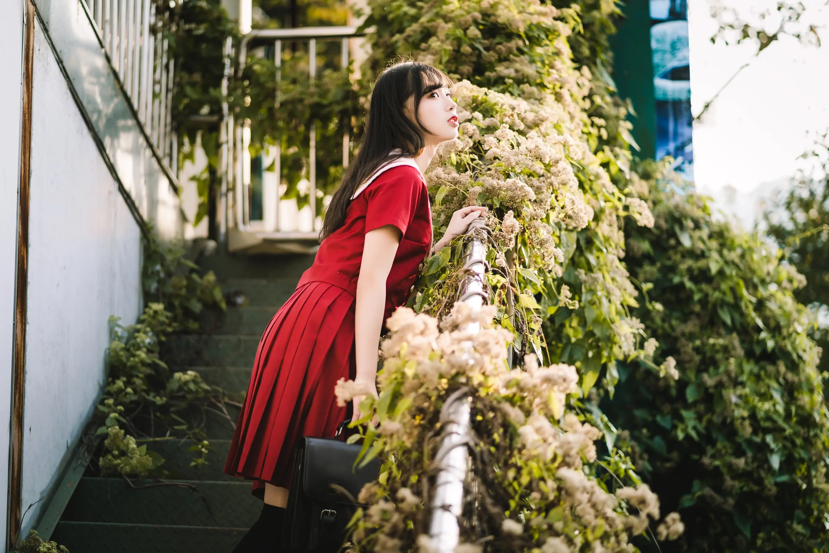 身穿红色连衣裙的 araffe 女子靠在种满植物的栏杆上