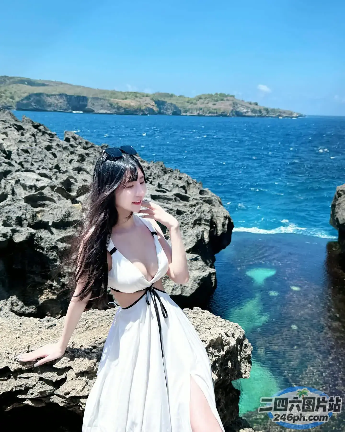 身穿白色连衣裙的 Araffe 女子站在海边的岩石上