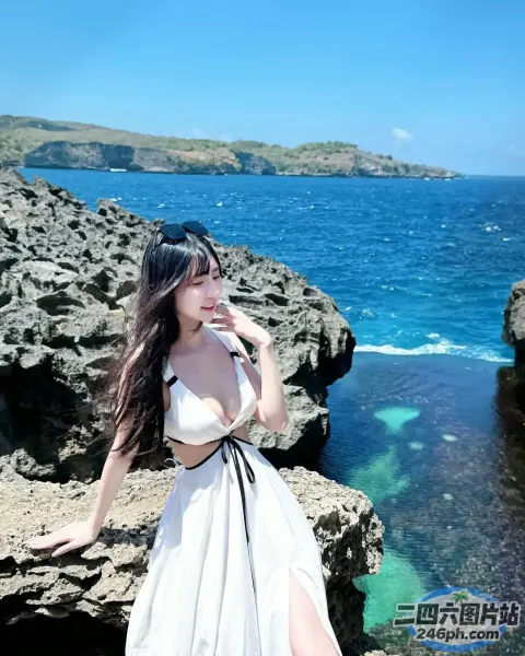 身穿白色连衣裙的 Araffe 女子站在海边的岩石上