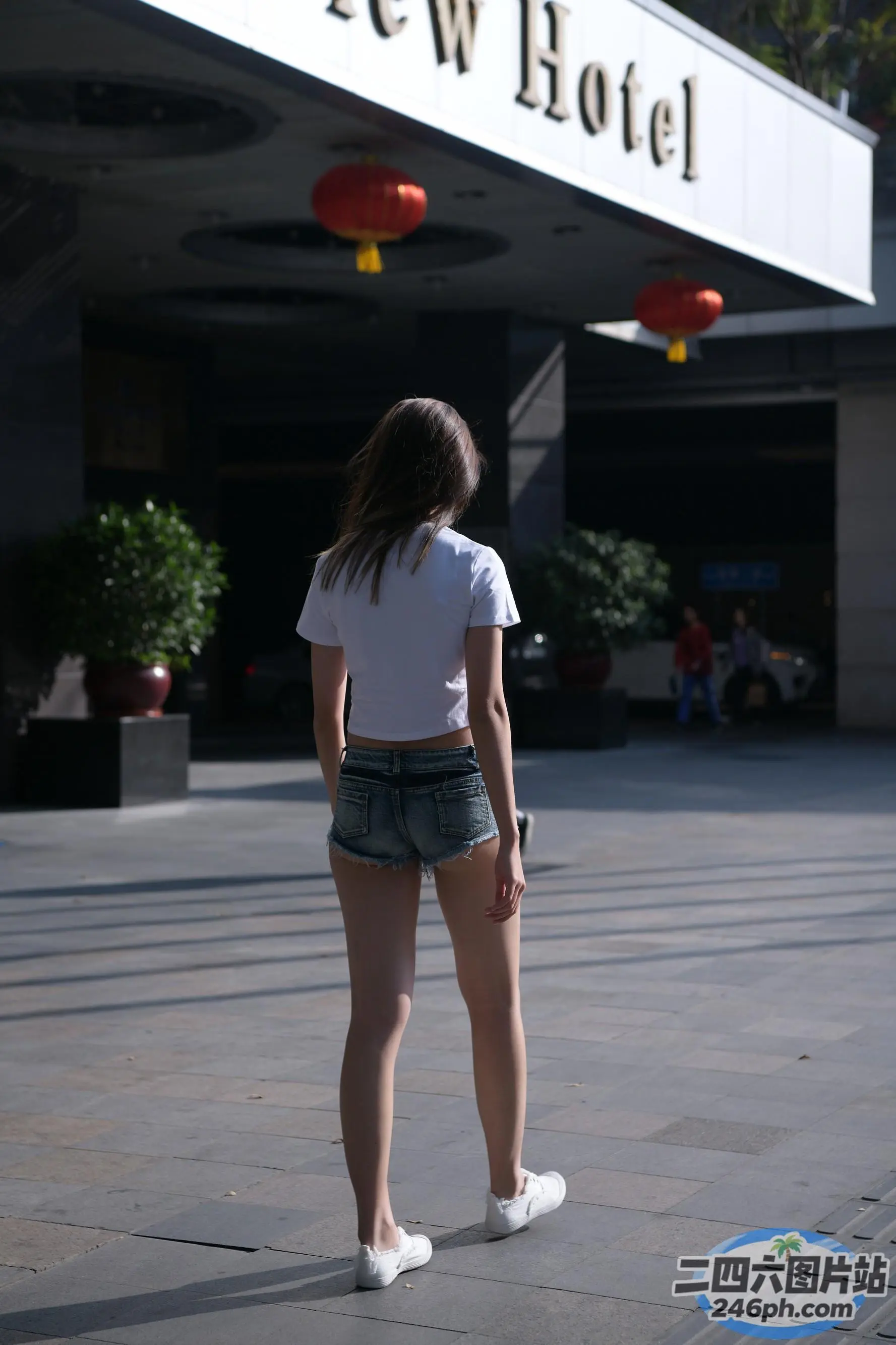 身穿短裤和白衬衫的 arafed 女子站在酒店门前