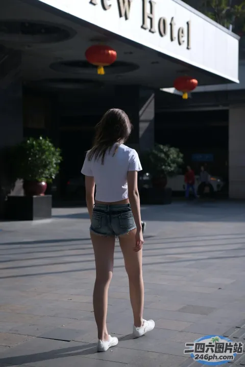 身穿短裤和白衬衫的 arafed 女子站在酒店门前