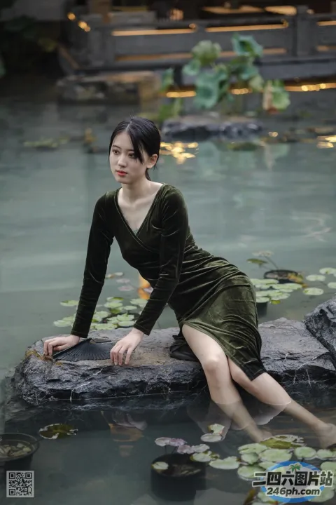 穿着绿色连衣裙的 arafed 女人坐在池塘的岩石上