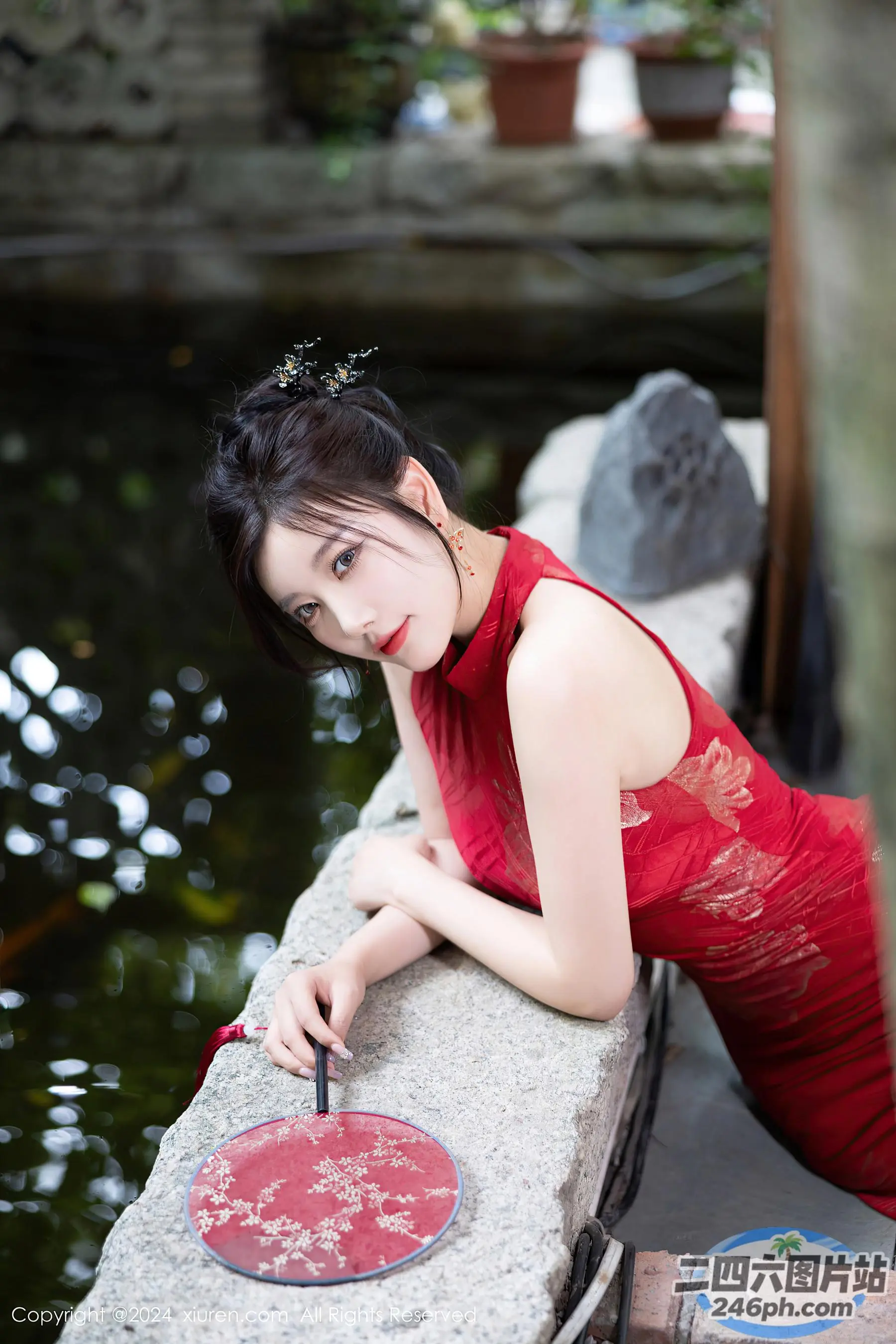 身穿红色连衣裙的 arafed 亚洲女子靠在池塘附近的墙上