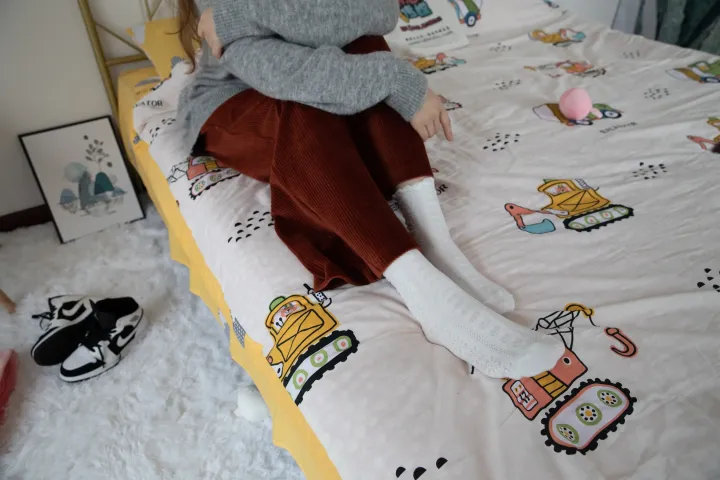 有一个小女孩坐在床上，床上盖着一条毯子