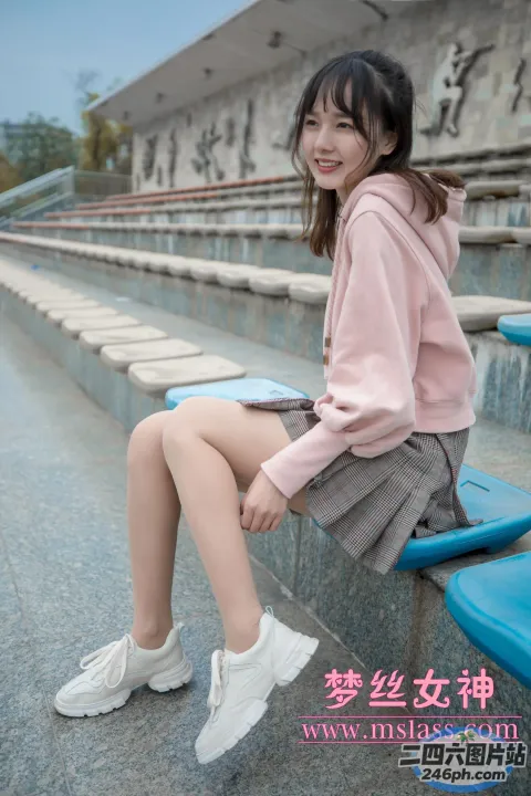 一名身穿粉红色连帽衫的女子坐在体育场的长凳上