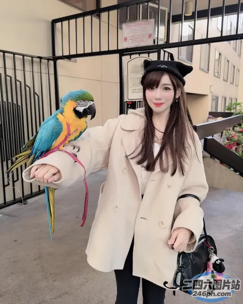 女子站在建筑物前，手臂上抱着一只鹦鹉