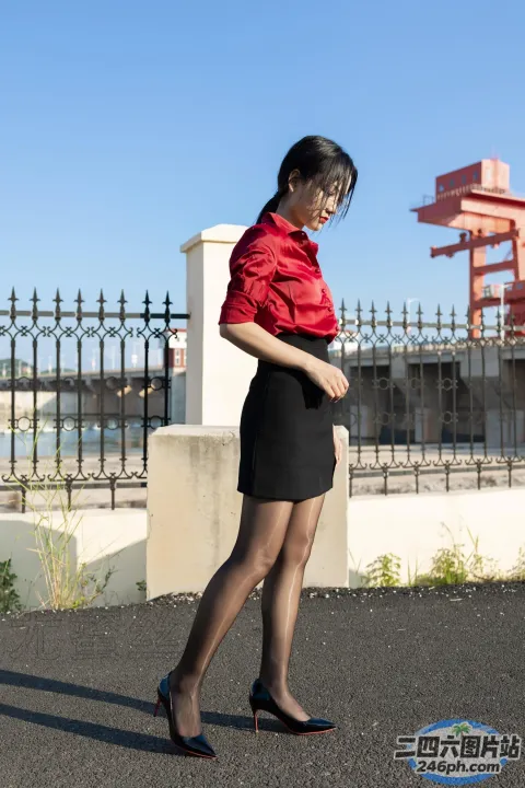 身穿红色衬衫和黑色裙子的女子在栅栏附近的人行道上行走