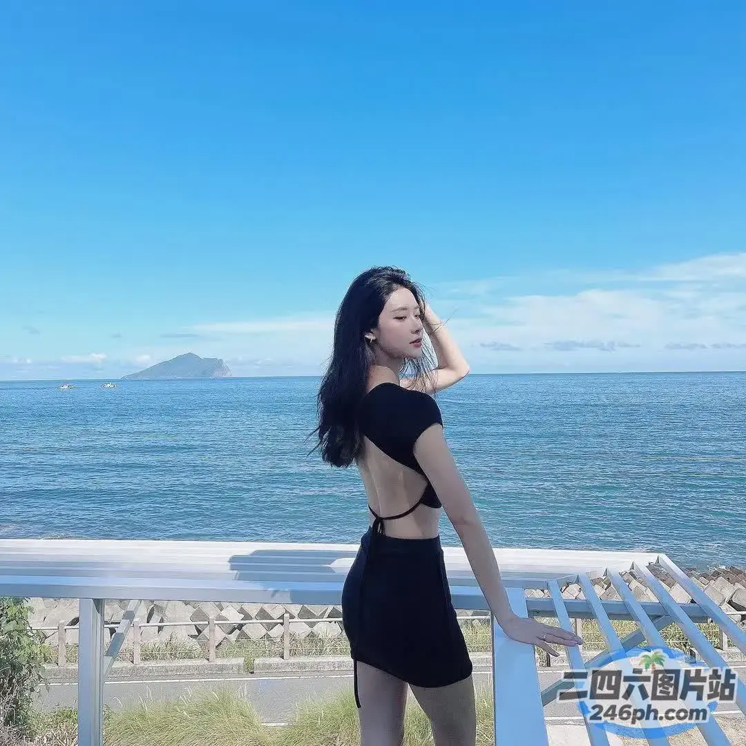 身穿黑色连衣裙的 araffe 女子站在俯瞰大海的阳台上