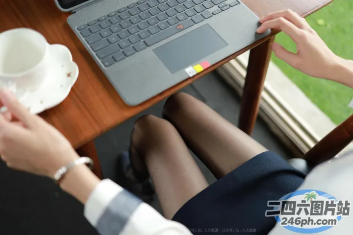 有人坐在桌子旁，手里拿着笔记本电脑和一杯咖啡