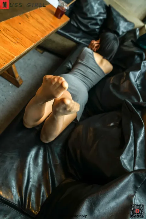 有一个人躺在黑色的皮沙发上，双脚抬起