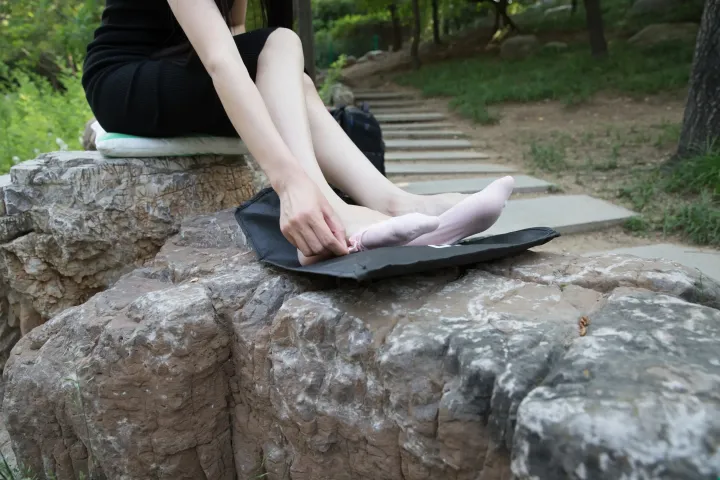 有个女人坐在石头上，脚踩在笔记本电脑上