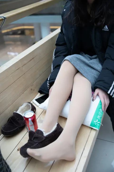 女人坐在长凳上，脚踩着一罐苏打水