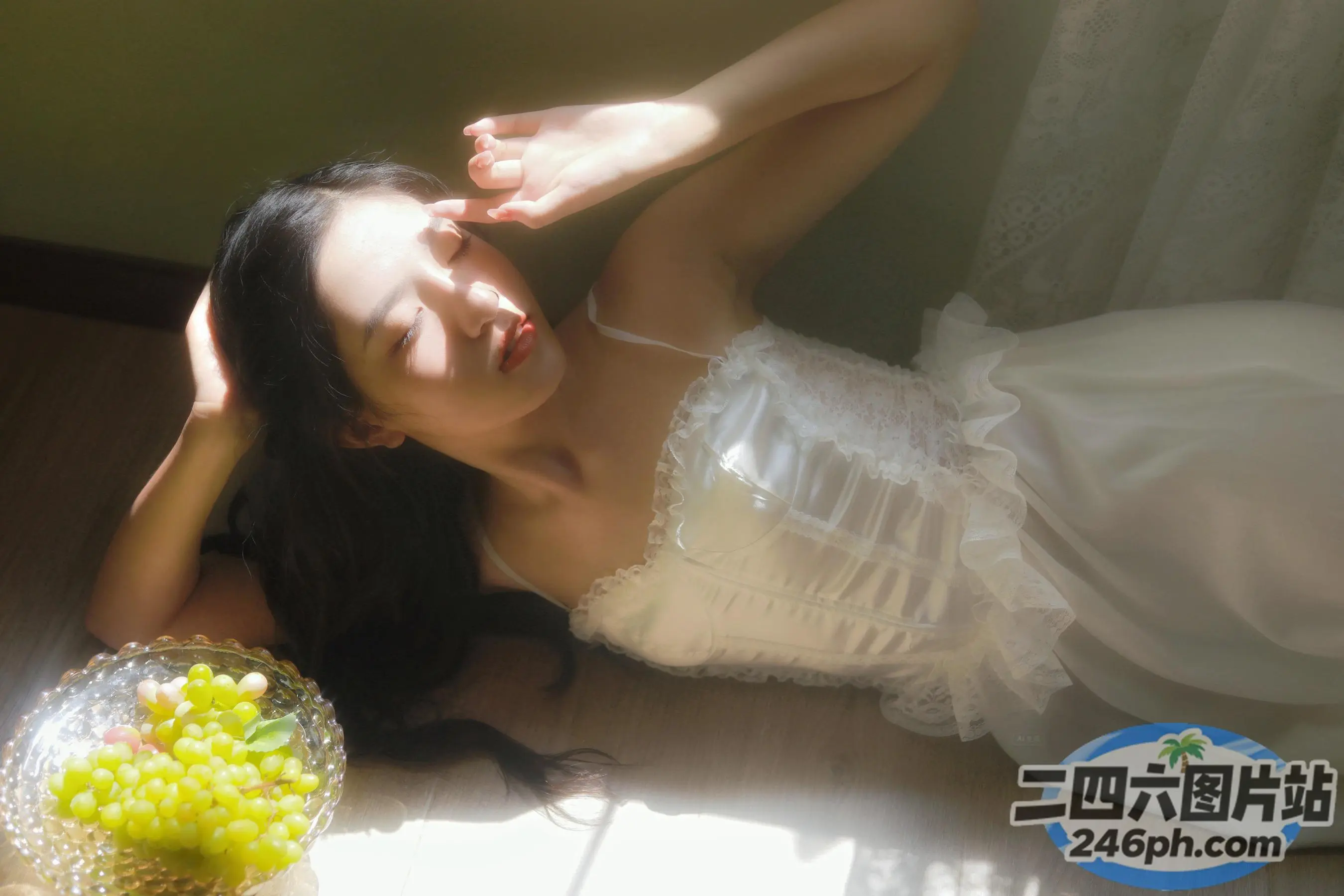 穿着白色连衣裙的 Arafed 女人躺在地板上，旁边是一碗葡萄