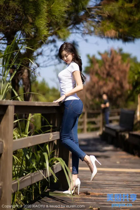 身穿白衬衫和蓝色牛仔裤的亚洲女性靠在木栅栏上