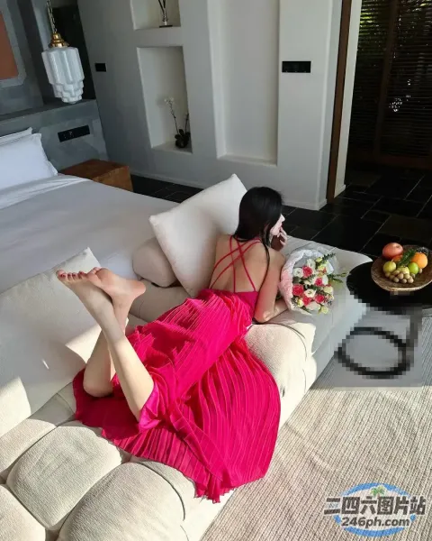 穿着粉红色连衣裙的女人躺在沙发上，手里拿着一盘水果