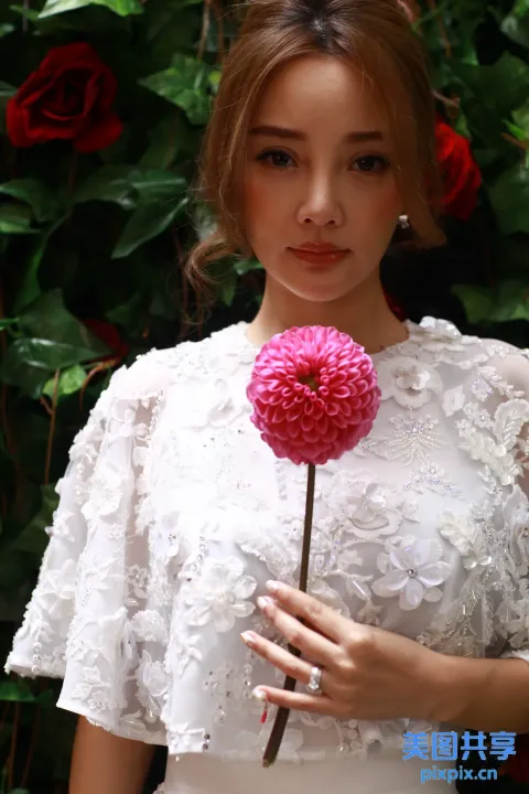 有一个女人在灌木丛前捧着一朵花
