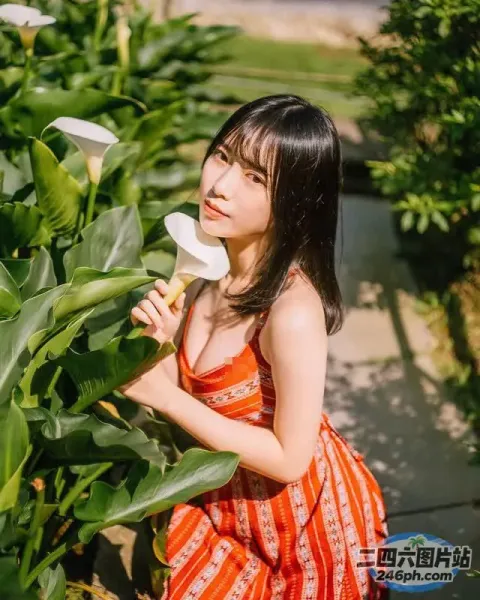 一个穿着裙子的女人在灌木丛前拿着一朵花