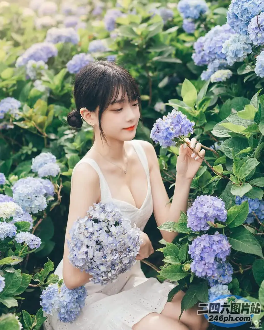 一个穿着白色连衣裙的女人坐在开着蓝色花朵的灌木丛中