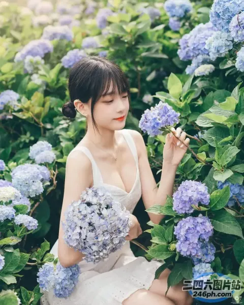 一个穿着白色连衣裙的女人坐在开着蓝色花朵的灌木丛中