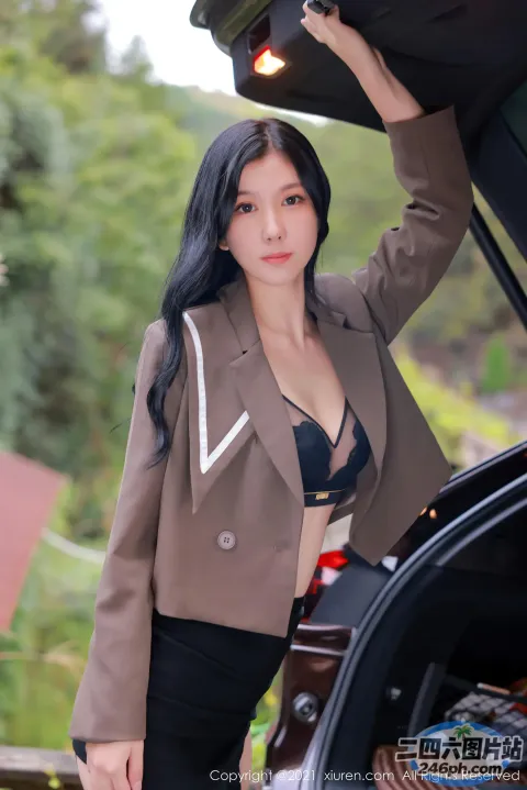 身穿棕褐色夹克和黑色裙子的女子站在一辆汽车旁边