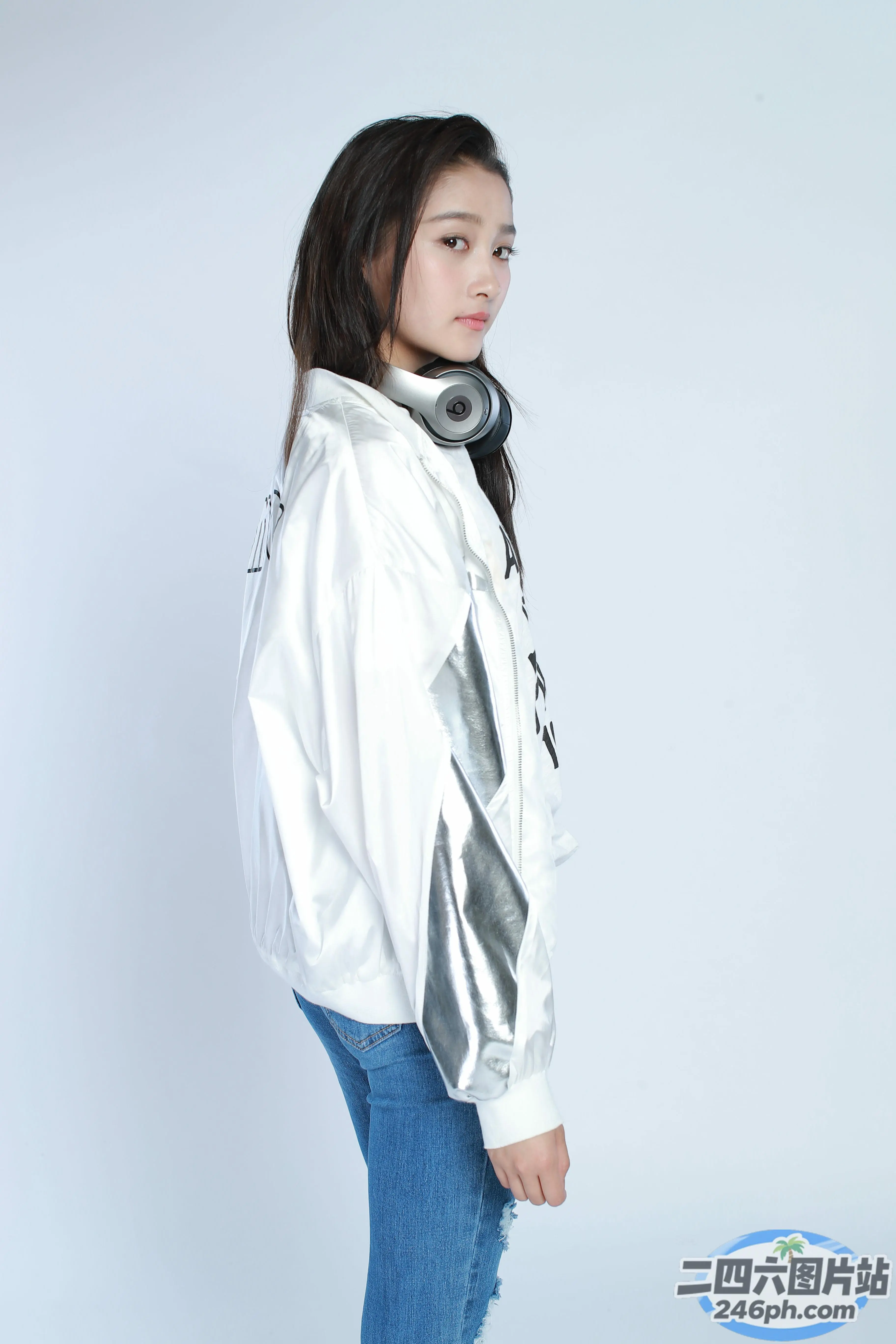 身穿白色夹克和牛仔裤的阿拉夫女人双手插在口袋里站着