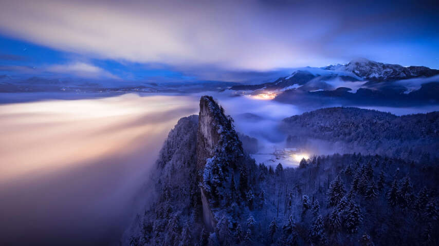 山被雪和雾覆盖，远处有一座灯塔