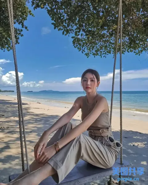 女人坐在海滩上的秋千上，手里拿着一本书