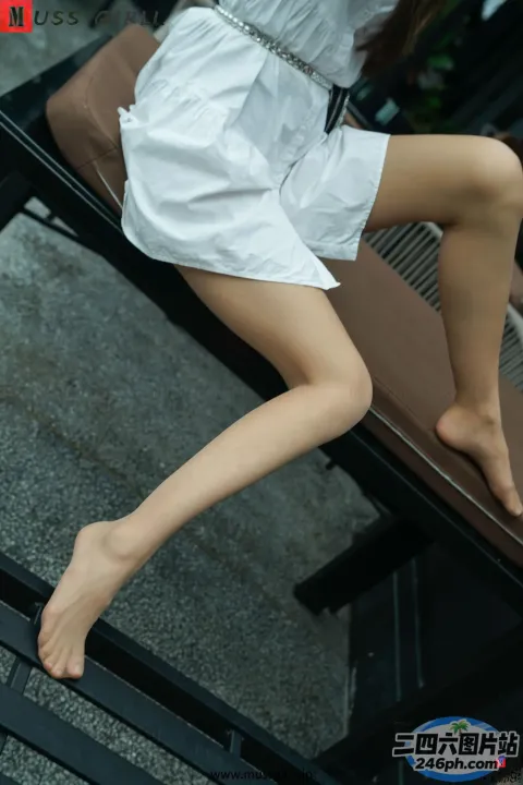 身穿白色连衣裙的 Araffed 女子双腿交叉坐在长凳上