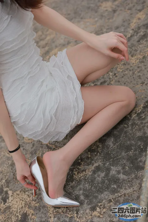 穿着白色连衣裙的 Araffed 女人系着她的银色高跟鞋