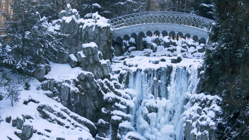 白雪皑皑的瀑布，背景是一座桥，前景是树木