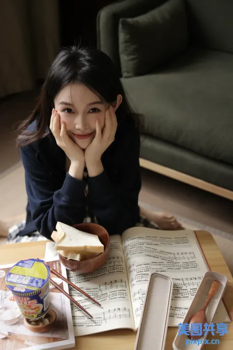 地板上坐着一个女人，手里拿着一本书和一碗食物