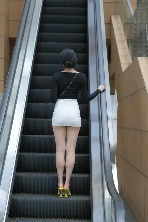 穿着裙子的 Araffe 女子乘坐自动扶梯从楼梯上下来