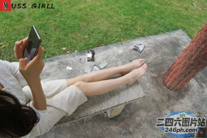 女子双腿交叉坐在长凳上，手里拿着手机