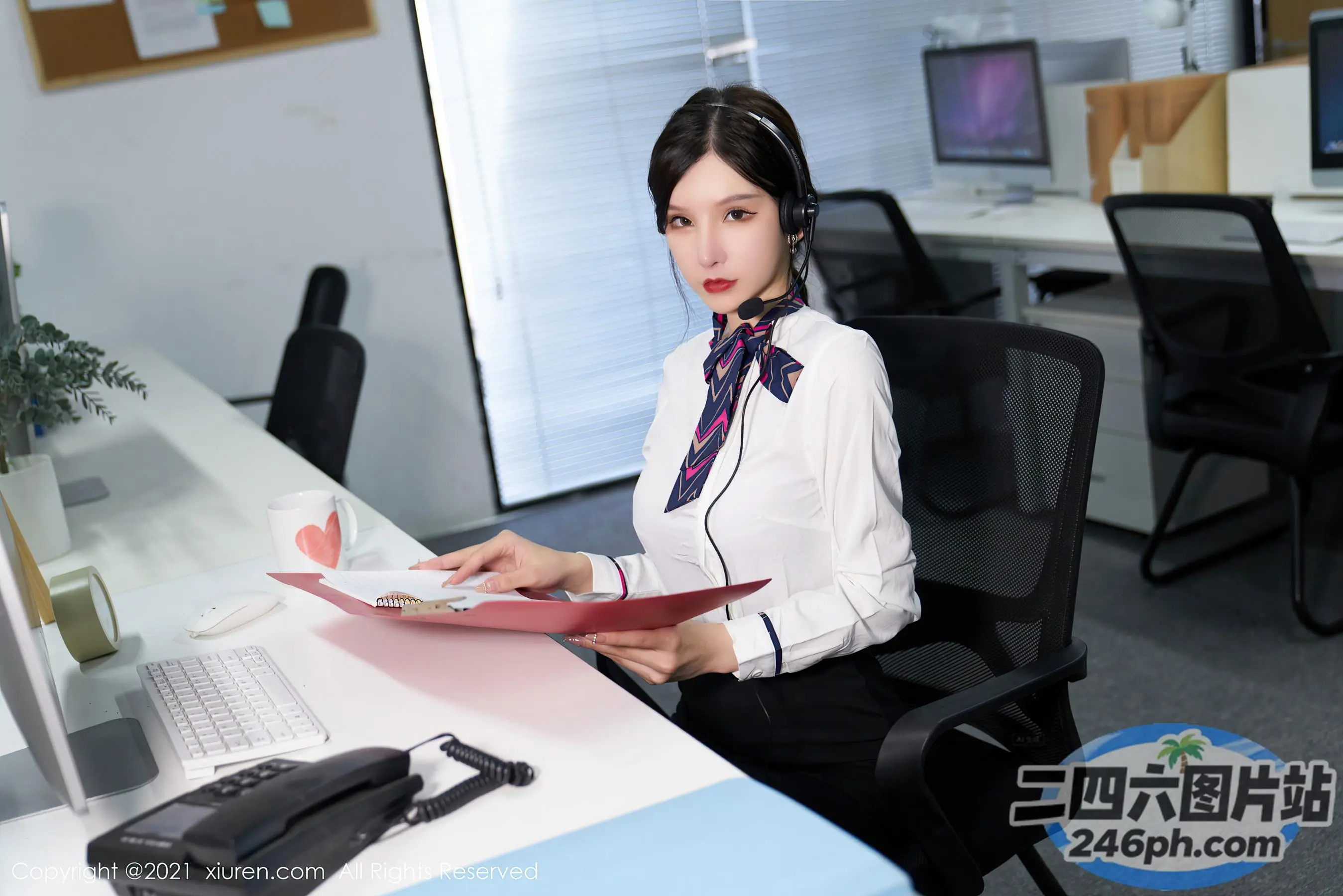 书桌前坐着一个女人，手里拿着一本书和一台电脑