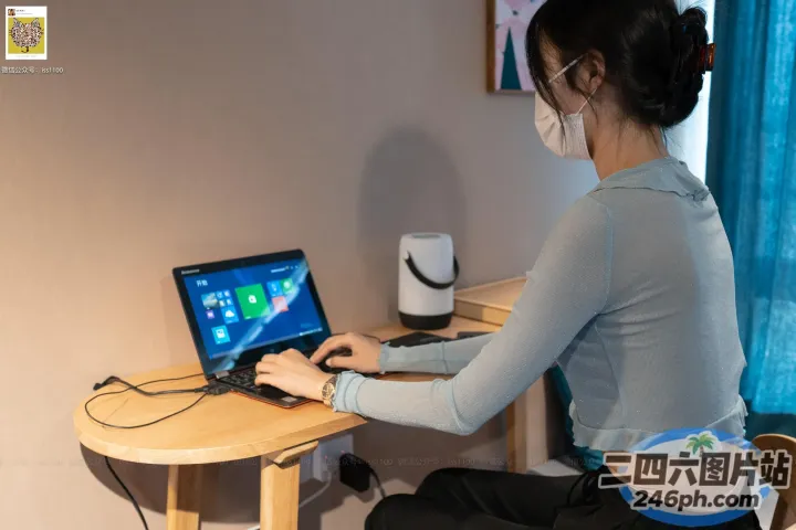 戴着口罩坐在办公桌前使用笔记本电脑的女士