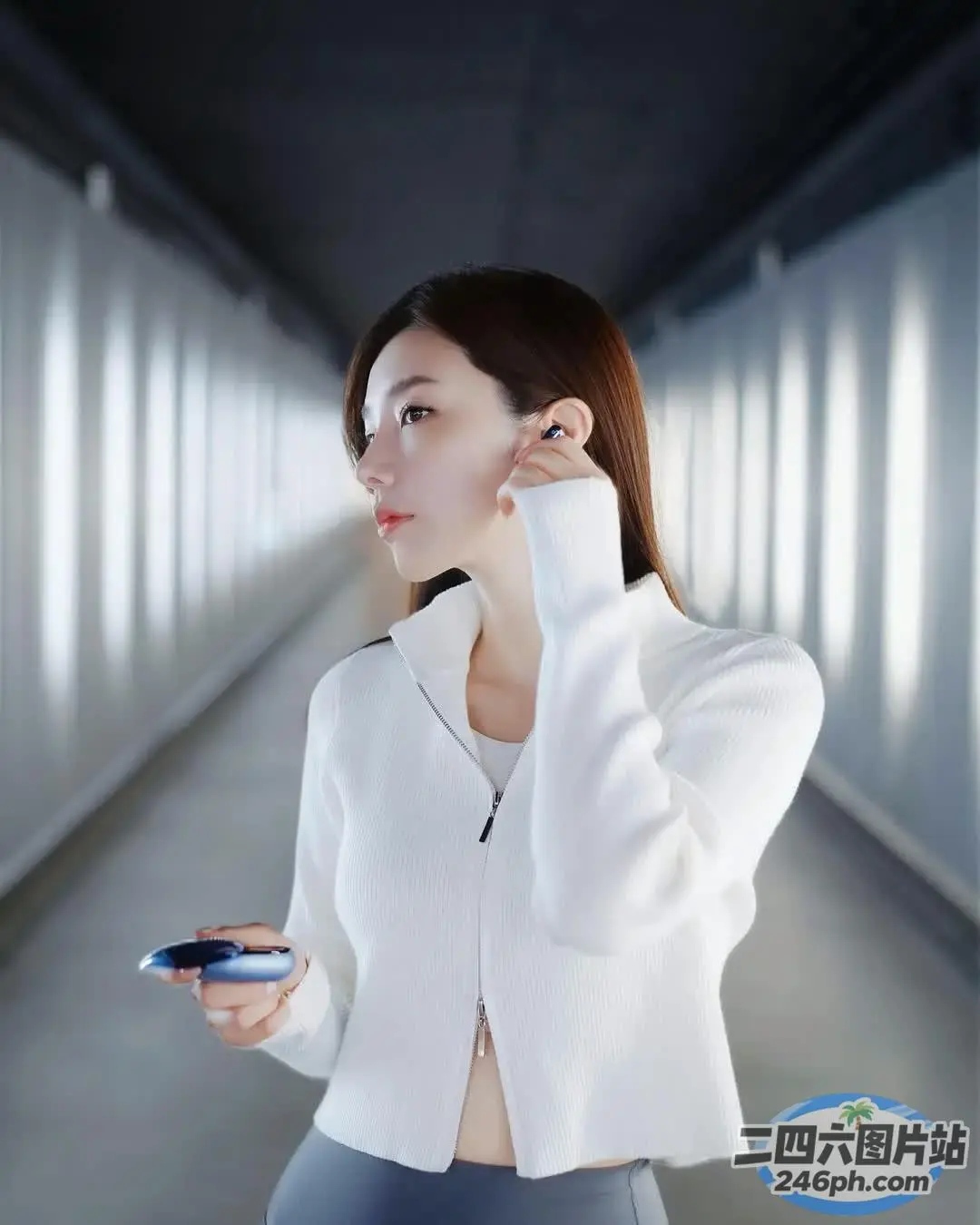 身穿白色夹克的 Arafed 女子在走廊上拿着手机